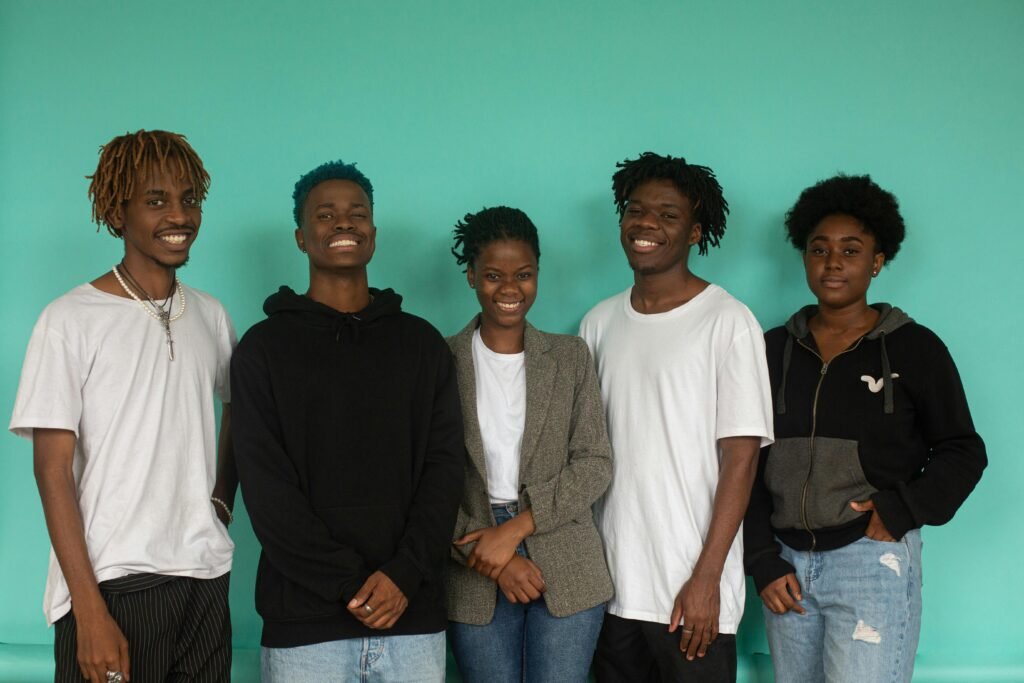 A diverse group of five young adults smiling against a teal background in a studio setting.